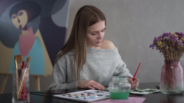 Talented Beautiful Woman Painting Sitting at Table and Looking at Camera Smiling