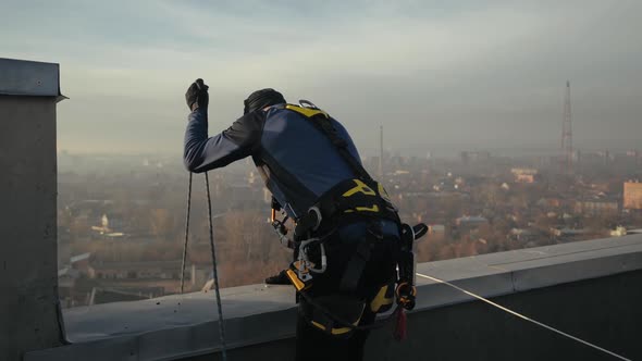 Rear Shot of Sports Industrial Climber, Man in Special Uniform Standing on Roof, Slowly Lowering the