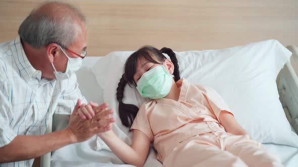 Asian young little girl kid wearing mask lying on bed in recovery room from curing COVID with daddy.