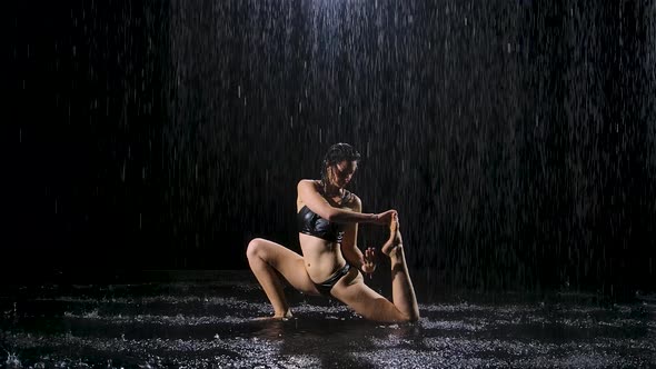 A Young Woman Doing Stretching Exercises Under the Streams of Rain. Drops of Water Fall on Body