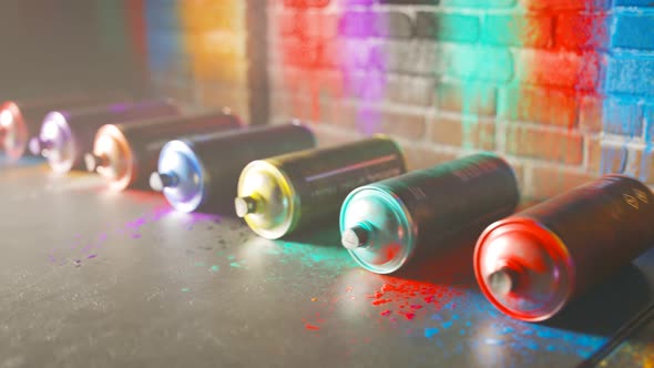 Used, colorful spray paint cans rolling in front of a painted brick wall. 4KHD