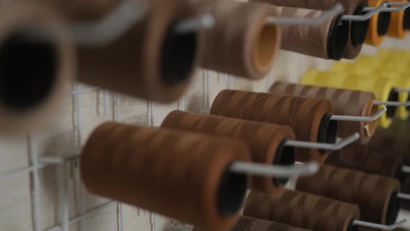 A set of colored threads for sewing on reels on the wall in the sewing workshop. Side view