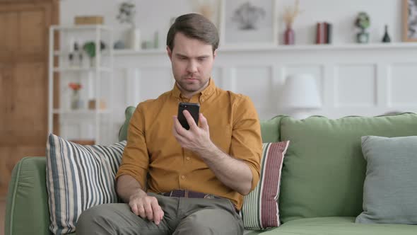 Young Man having Loss on Smartphone at Home