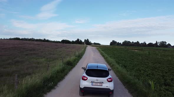 White car driving slow on a dirt road between the farm fields in Scherpenheuvel, Belgium.