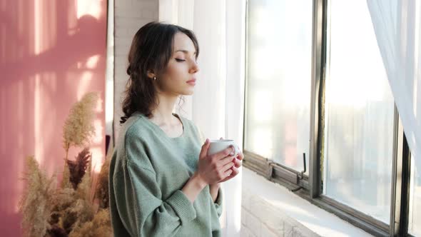 Beautiful Woman Sitting Near Window and Enjoy a Cupt of Tea on Background of Sunrise