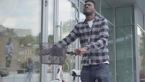 Handsome Confident African American Man in Casual Clothes Leading His Bicycle Near the Shop Windows