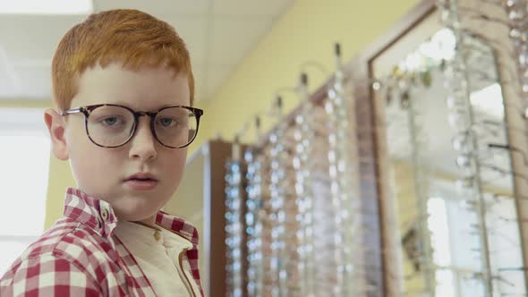 A Very Funny Boy in a Red and White Shirt Stands in the Optics with Glasses for Vision Correction