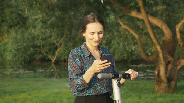 Portrait of attractive woman in shirt is using alternative electric scooter in park. E-transport