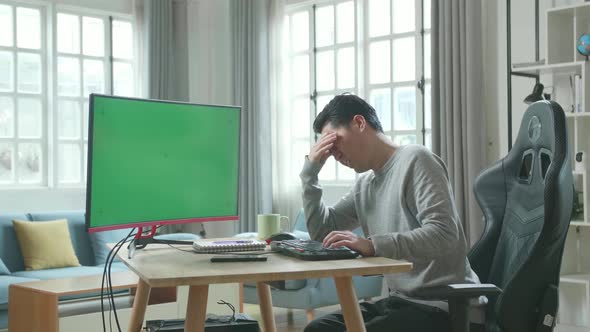 Asian Man Being Tired While Using Green Screen Desktop Computer For Working At Home