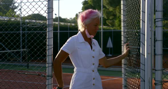 Girl with White and Short Hair Close-up, She Stands Against the Fence in a Mesh on a Sunny Day