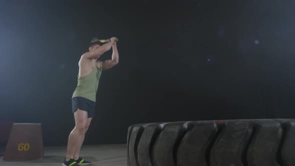 Strong Sportsman Hitting Tire with Sledgehammer