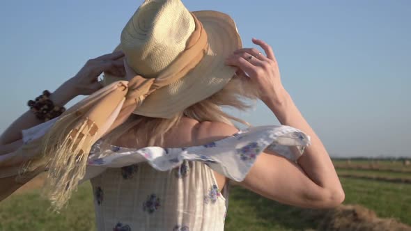 Young Happy Rural Woman in a Straw Hat and Summer Dress on the Background of a Green Field