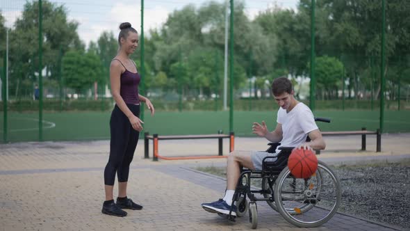 Wide Shot Happy Girlfriend Playing Basketball with Boyfriend in Wheelchair Outdoors