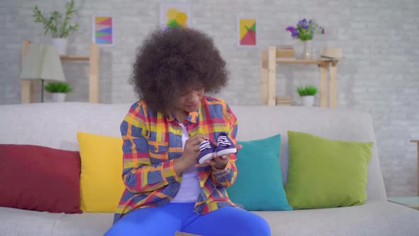 Joyful and Happy African American Woman with an Afro Hairstyle Unpacks the Parcel Sitting