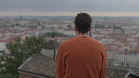 A young man sitting in front of a beautiful view of the city of Lyon in France.