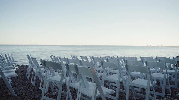 Rows of white folding chairs set up on the shoreline of a body of water