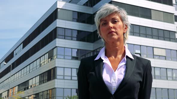 Business Middle Age Woman Looks To Camera with Serious Face As Boss - Company Building