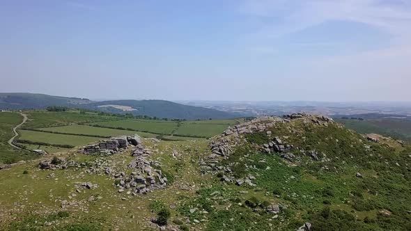 Wide shot aerial tracking forward upwards above Sharps Tor to reveal a wide expanse of countryside,