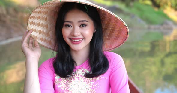 Vietnamese Girl With Traditional Dress And Hat On Boat And Looking At Camera