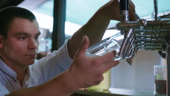 Professional Bartender Pours Fresh Cool Light Draft Beer Into a Glass Using Pour From Keg