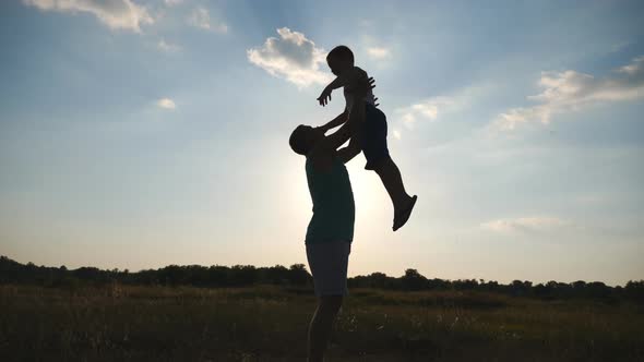 Happy Daddy Throwing Up His Little Boy in the Air at Nature. Silhouettes of Father and Son Playing