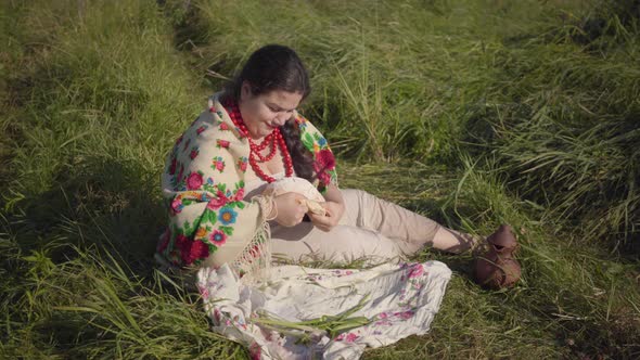 Beautiful Overweight Woman Sitting in Grass on the Field Eating a Piece of Fresh Bread