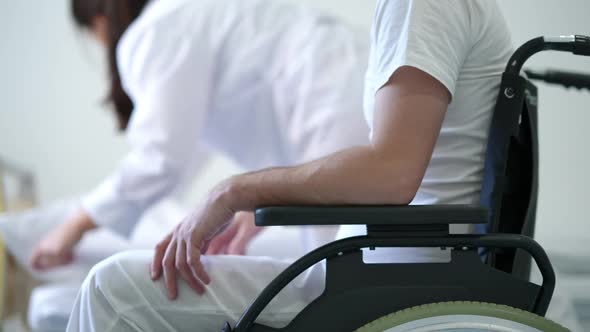 Unrecognizable Man in Wheelchair Waiting for Nurse Making Bed at Background