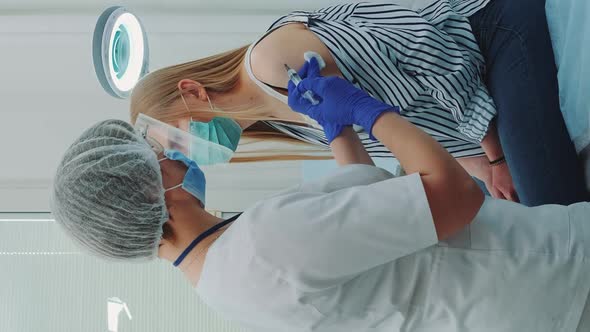 Female Doctor in Medical Protective Cloths Injecting in Woman's Arm a Vaccine Against Coronavirus