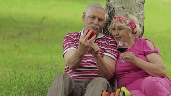 Family Picnic. Senior Old Grandparents Couple in Park Using Smartphone Online Browsing, Shopping