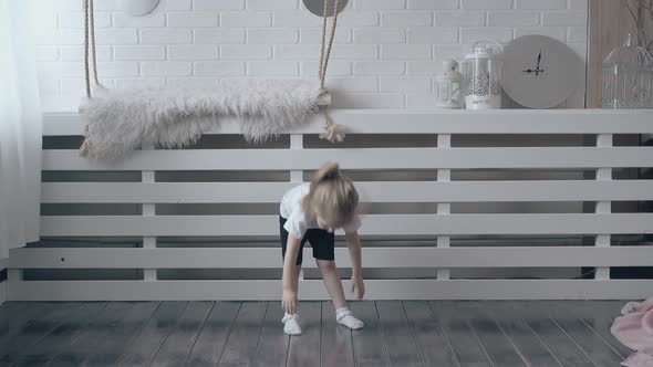 Little Blond Girl Leans Forward and Touches Wooden Floor