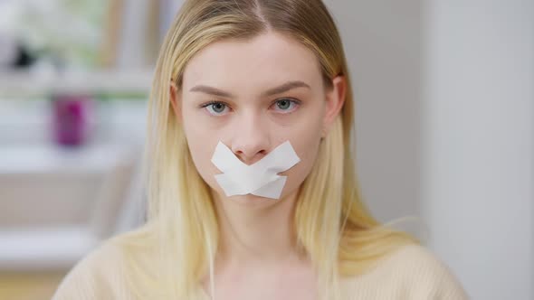 Closeup of Young Discriminated Woman with Taped Mouth Looking at Camera