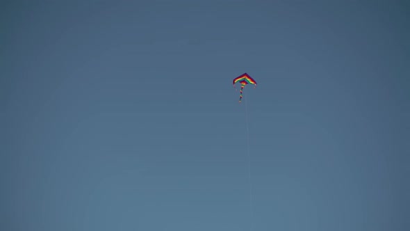 A Multicolored Kite Flying High in the Blue Sky Under the Gusts of Wind