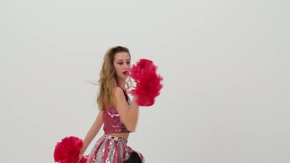 Young Cheerleader with Red Pompoms in Uniform is Dancing on White Background in Studio