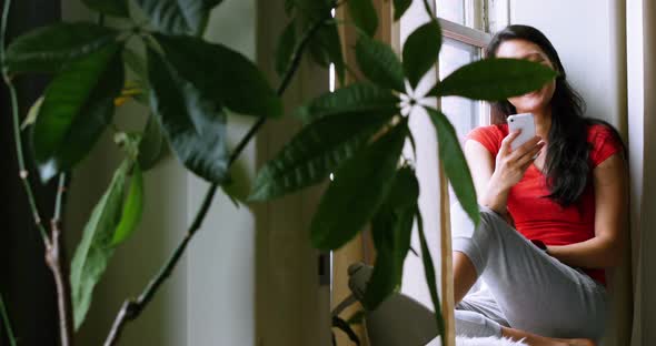 Woman sitting on windowsill and using mobile phone