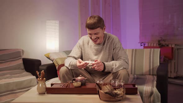 A Young Man at Home Cleans Dishes for a Special Tea Ceremony with a Towel, Smiles and Talks To a