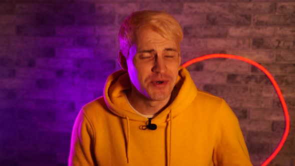 Young Man with Lavalier Microphone Talking on Camera Against Illuminated Brick Wall