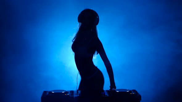 Silhouette of Model Woman DJ in the Smoke Mixes Music