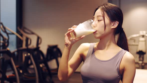 Attractive fitness asian woman finishing workout and drinking protein milk