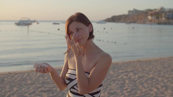 Woman Applying Sunscreen on Her Face Standing on the Beach