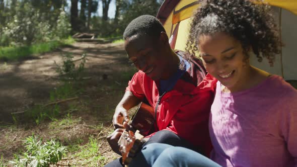 Smiling diverse couple sitting in tent and taking selfie in countryside