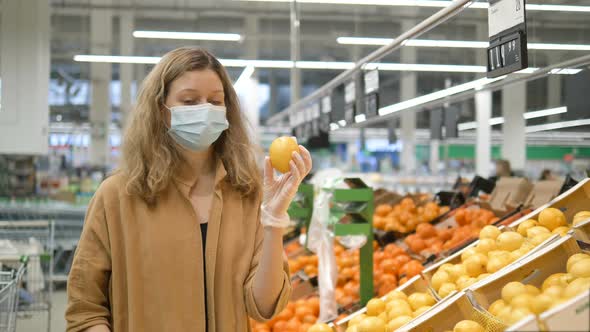 A Young Woman in a Medical Mask and Rubber Gloves Selects Fresh Lemons in a Grocery Supermarket