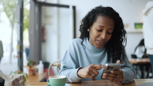 Pensive African woman wearing blue sweater leafing tape on phone