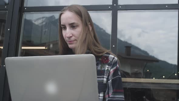 A Young Freelancer Girl Works at a Laptop in a Cafe Near the Mountains