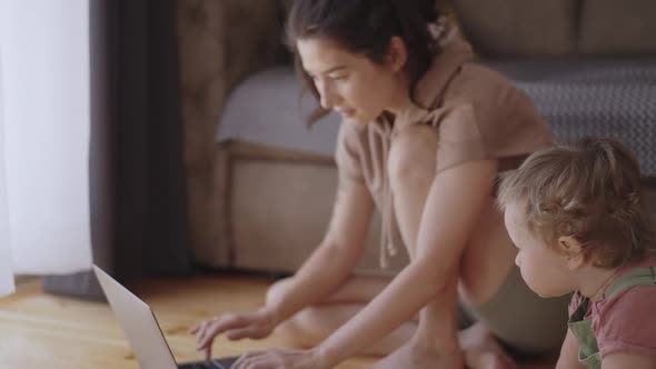 Mother Multitasking Holding Baby Infant and Using Computer Laptop at Home