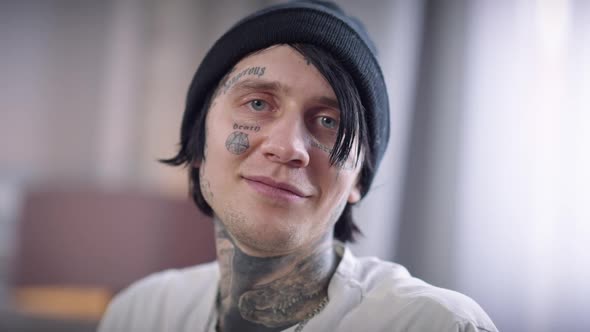 Closeup Tattooed Face of Young Man in Hat Looking at Camera Smiling