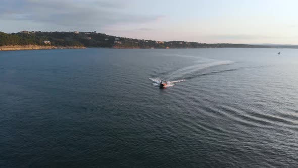 Backward pan shot of a boat pulling a tube on Lake travis revealing the cliffs in the background. Sh