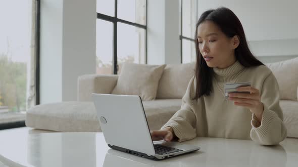 A Young Asian Woman Holding a Credit Card and Using a Laptop