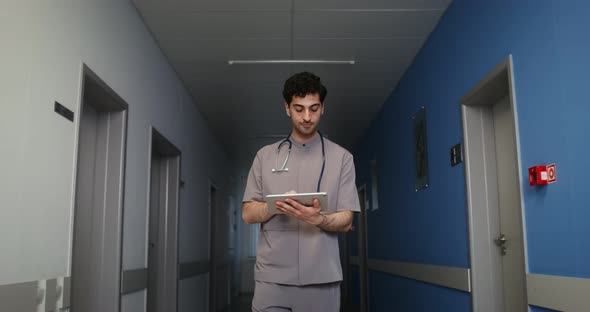 A Doctor Uses a Tablet While Walking Along the Corridor of the Hospital