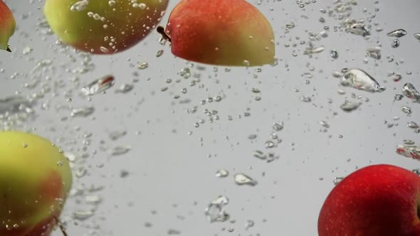 Apples Red and Yellow Under the Water Spinning and Rotating with Air Bubbles White Background