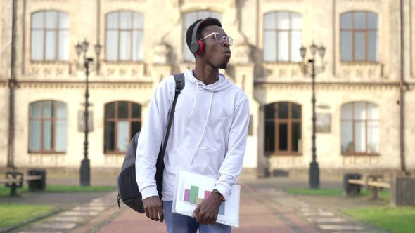 Self Assured Intelligent African American Young Student in Headphones Walking at Campus in Slow